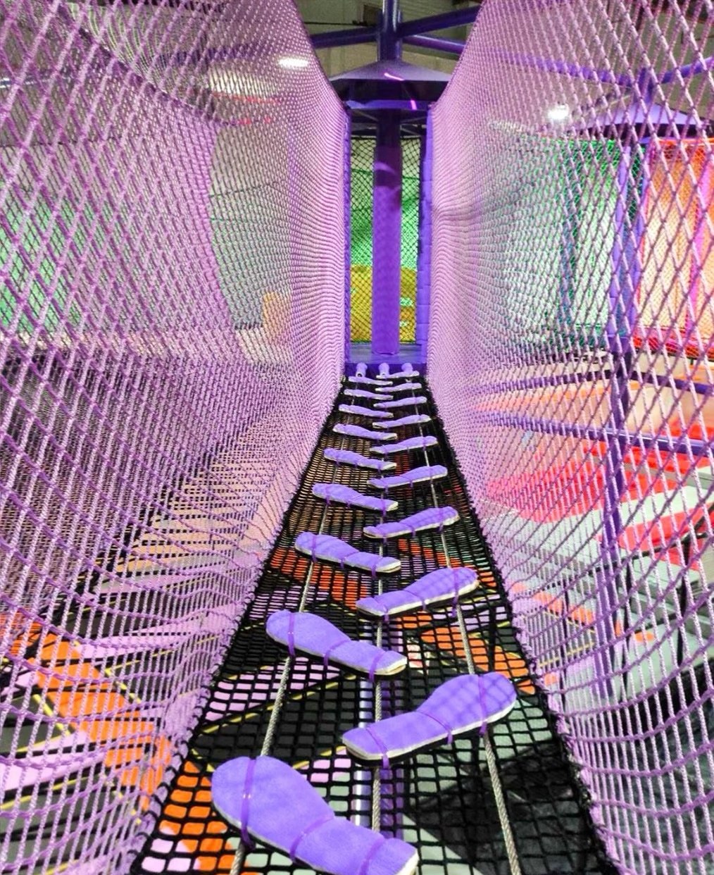 Purple net bridge adventure course inside a trampoline park