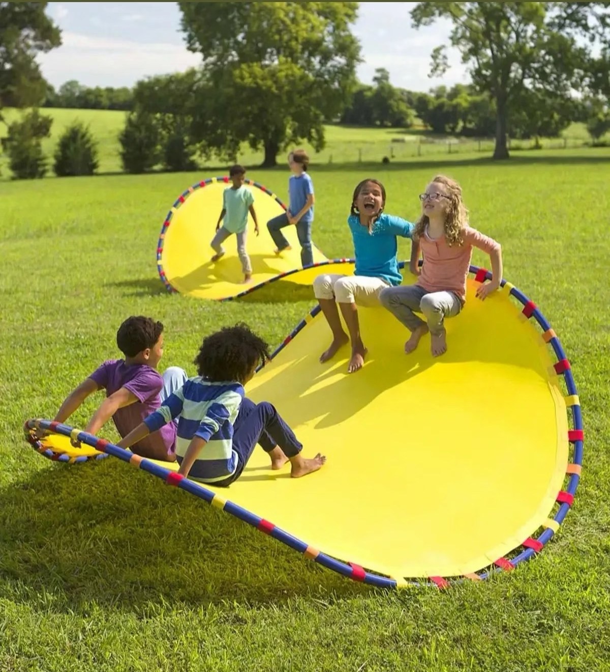 Children riding a giant yellow flex mat on grass