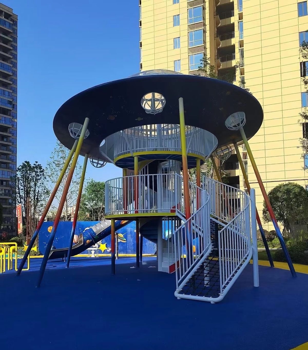 Flying-saucer play tower with slides on blue safety surfacing