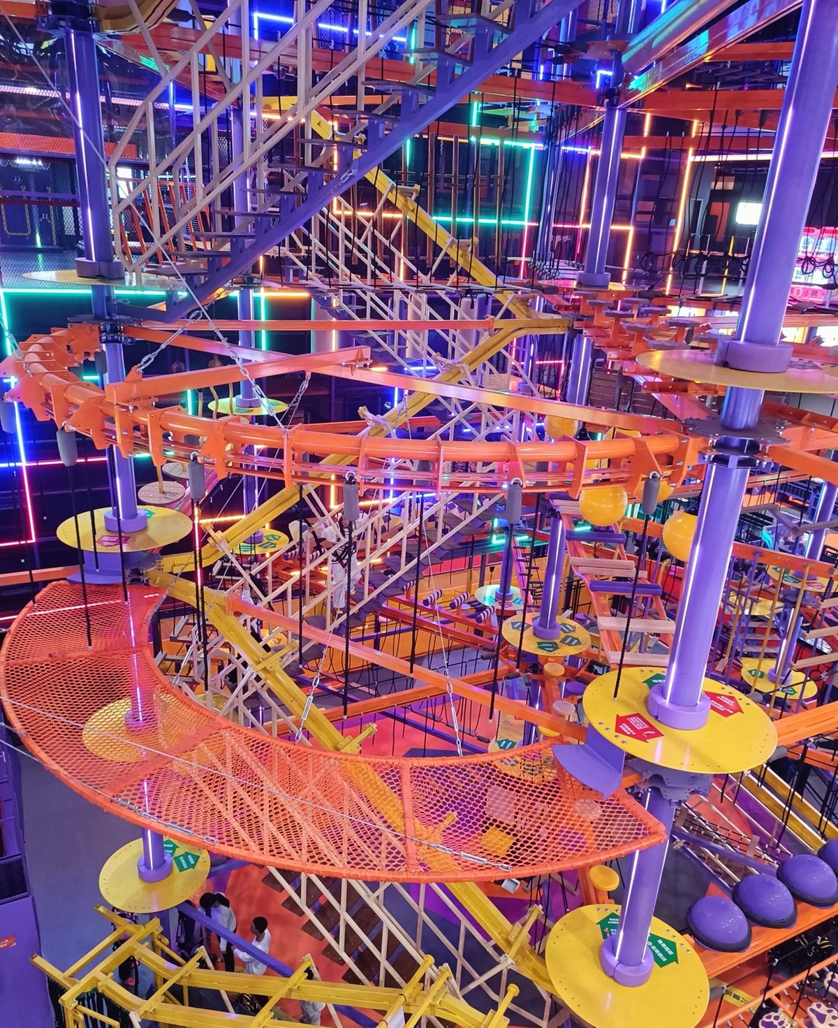 Multi-level indoor adventure course with nets under neon lights