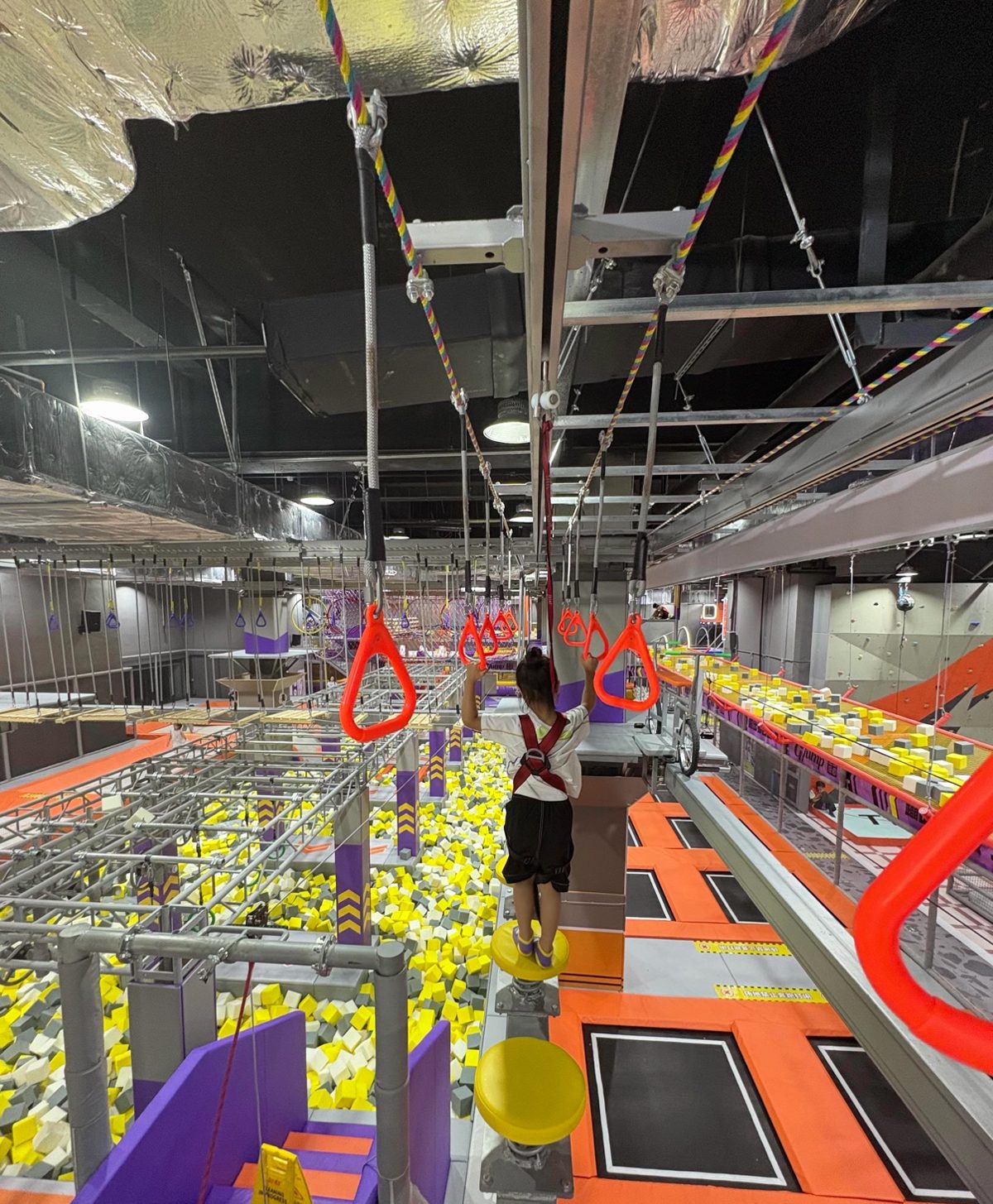 Child on an aerial ropes course with ring handles above trampolines and a foam pit