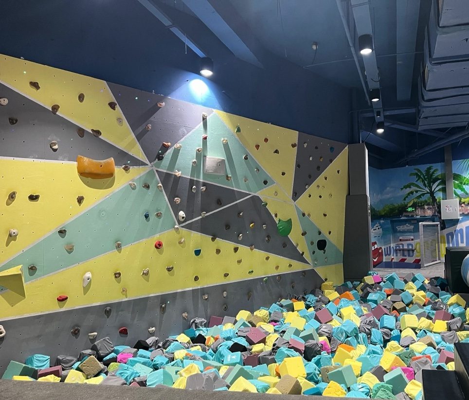 Geometric climbing wall in yellow and grey above a colourful foam pit