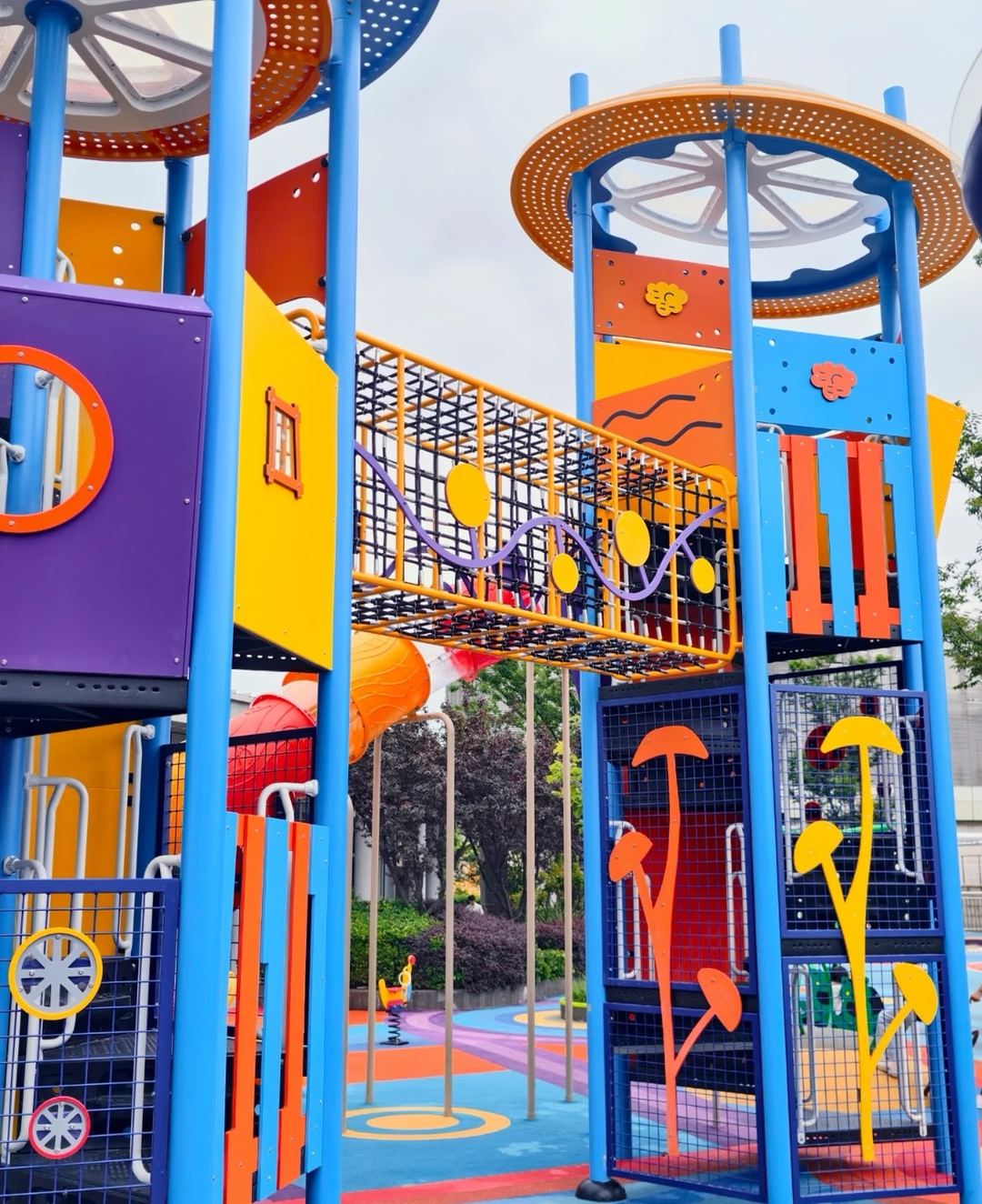 Colour-block outdoor play towers linked by a net bridge