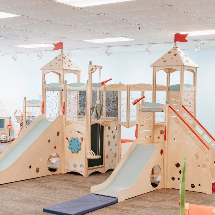 Low timber castle play system for kindergartens with slides and climbing panels